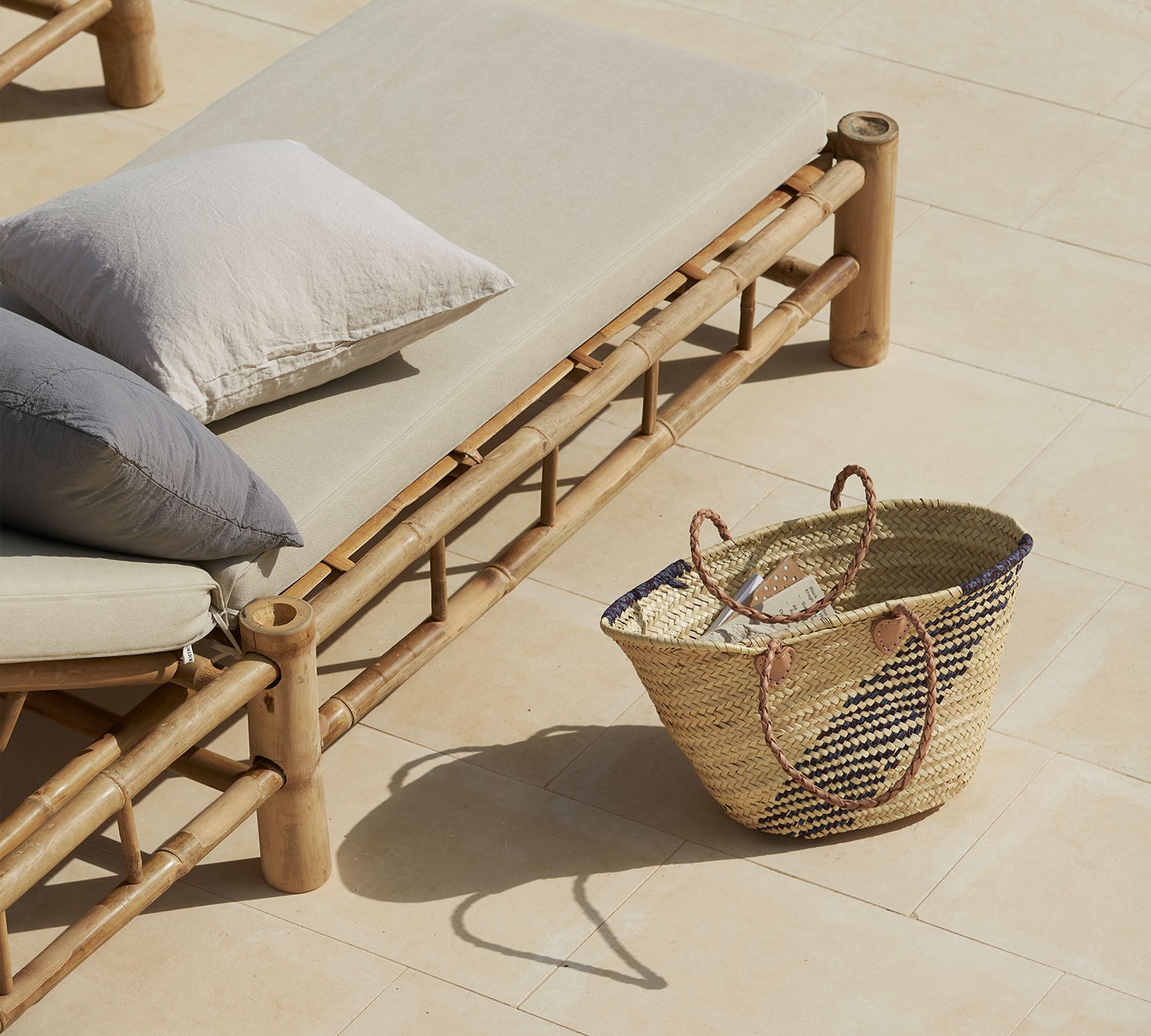 bamboo outdoor lounge with cushions and a woven basket on a tiled patio