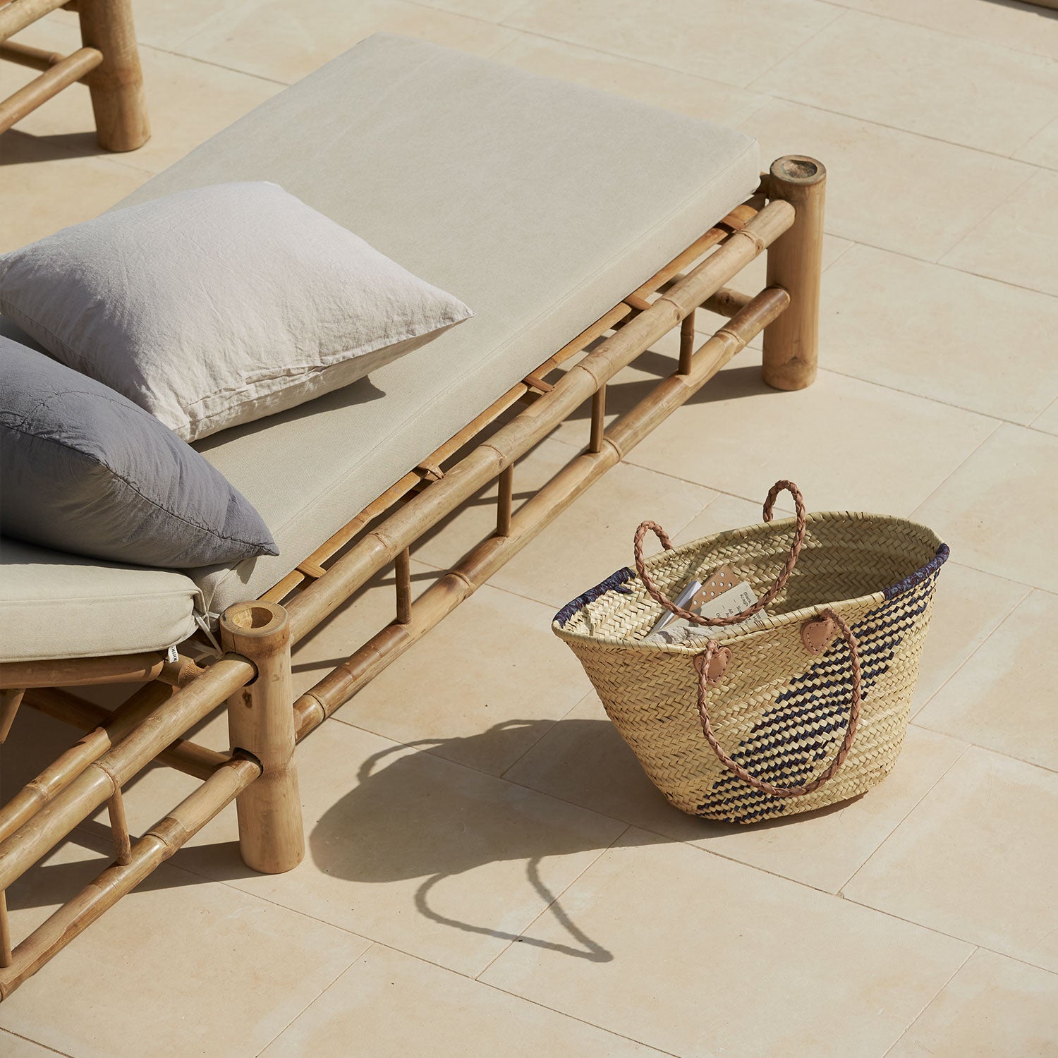 bamboo outdoor lounge with cushions and a woven basket on a tiled patio