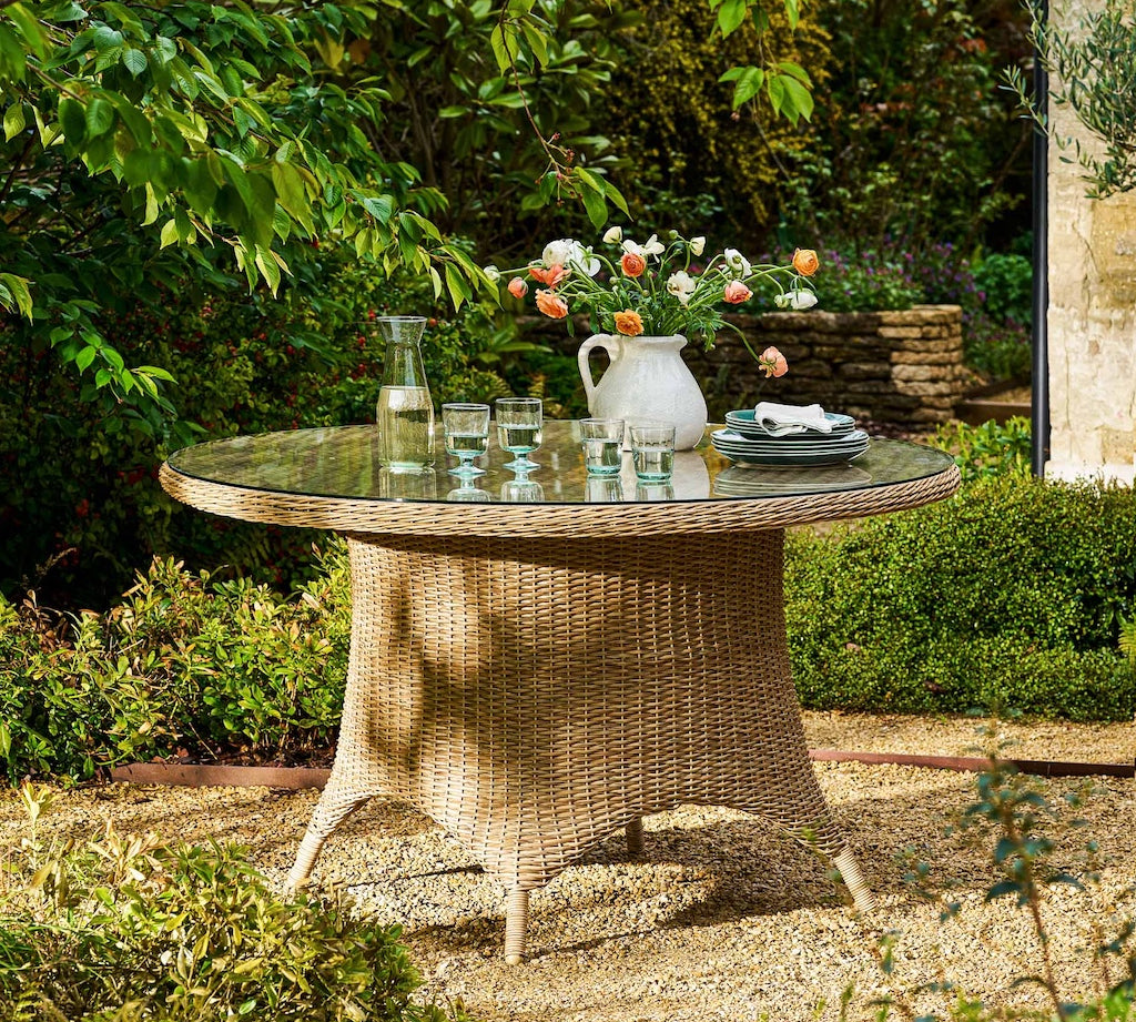 Round wicker table with a glass top set outdoors in a garden.