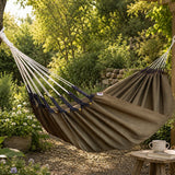 Brown hammock in a garden setting with a table and cup.