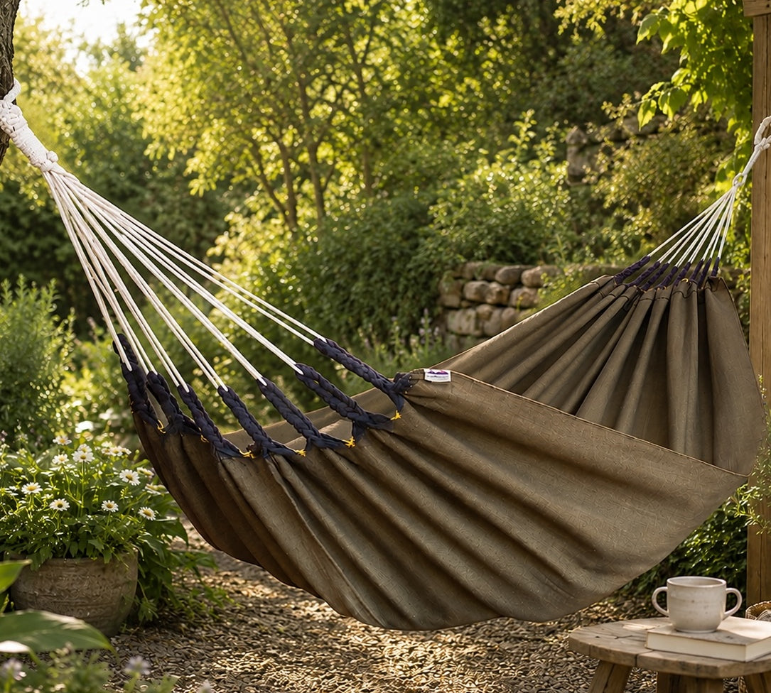 Brown hammock in a garden setting with a table and cup.