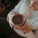 Person holding a terracotta mug with a warm hot chocolate beverage