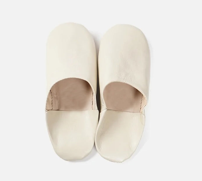 A pair of off-white leather slip-on slippers with a rounded toe and a low-cut vamp, shown from a top-down view on a light gray background.