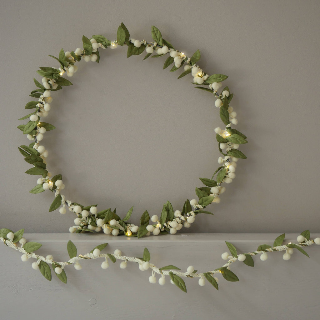 Decorative wreath with green leaves and white berries on a plain wall.