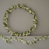 Decorative wreath with green leaves and white berries on a plain wall.