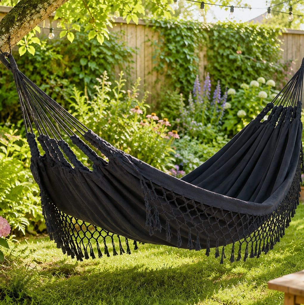 dark grey hammock hanging in a garden with greenery and flowers.