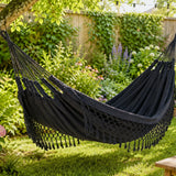 dark grey hammock hanging in a garden with greenery and flowers.