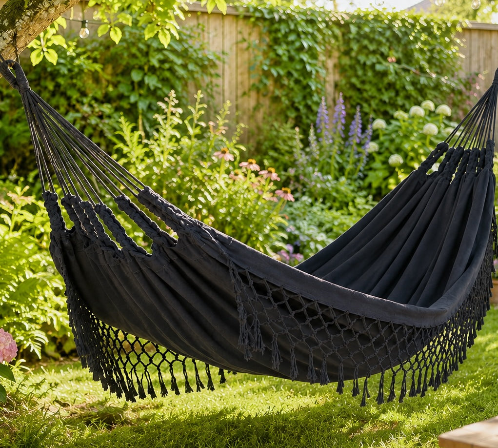 dark grey hammock hanging in a garden with greenery and flowers.