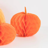 Bright orange honeycomb paper pumpkin decorations on a clean white background, with one main pumpkin in focus and part of another visible at the left edge.