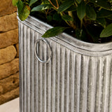 Metal planter with green plant against a stone wall background