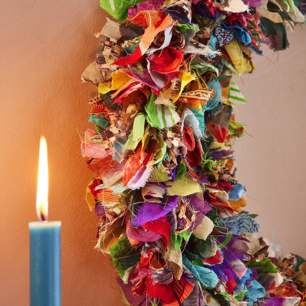 Colorful fabric wreath with a lit candle on a plain background