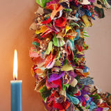 Colorful fabric wreath with a lit candle on a plain background