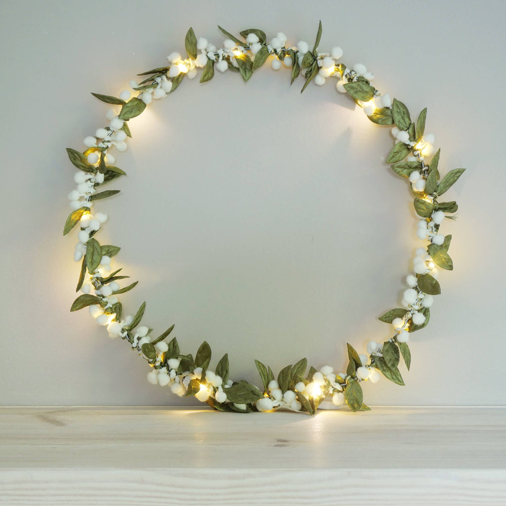 Decorative mistletoe wreath with green leaves and white berries on a plain background