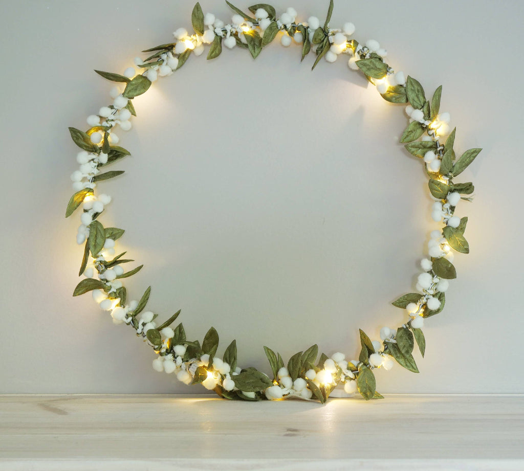 Decorative mistletoe wreath with green leaves and white berries on a plain background