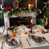 Decorated Christmas table with crackers, candles, and a bottle of champagne in front of a fireplace.