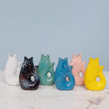 Set of colorful ceramic fish shaped vases on a marble surface with a light blue background