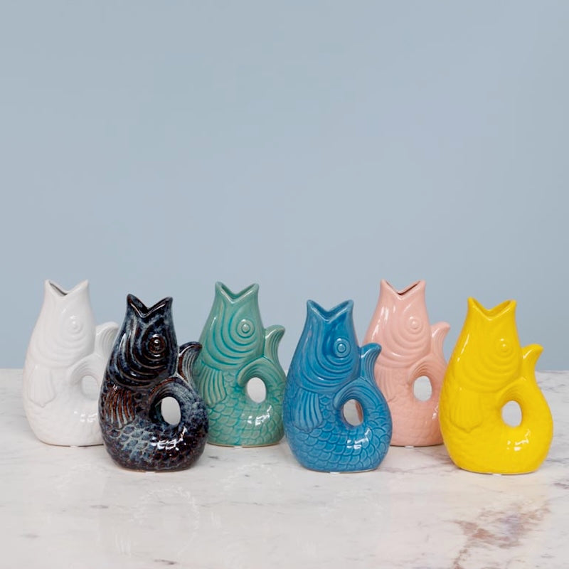 Set of colorful ceramic fish shaped vases on a marble surface with a light blue background