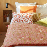 Bed with floral duvet and patterned pillows against a wooden headboard.