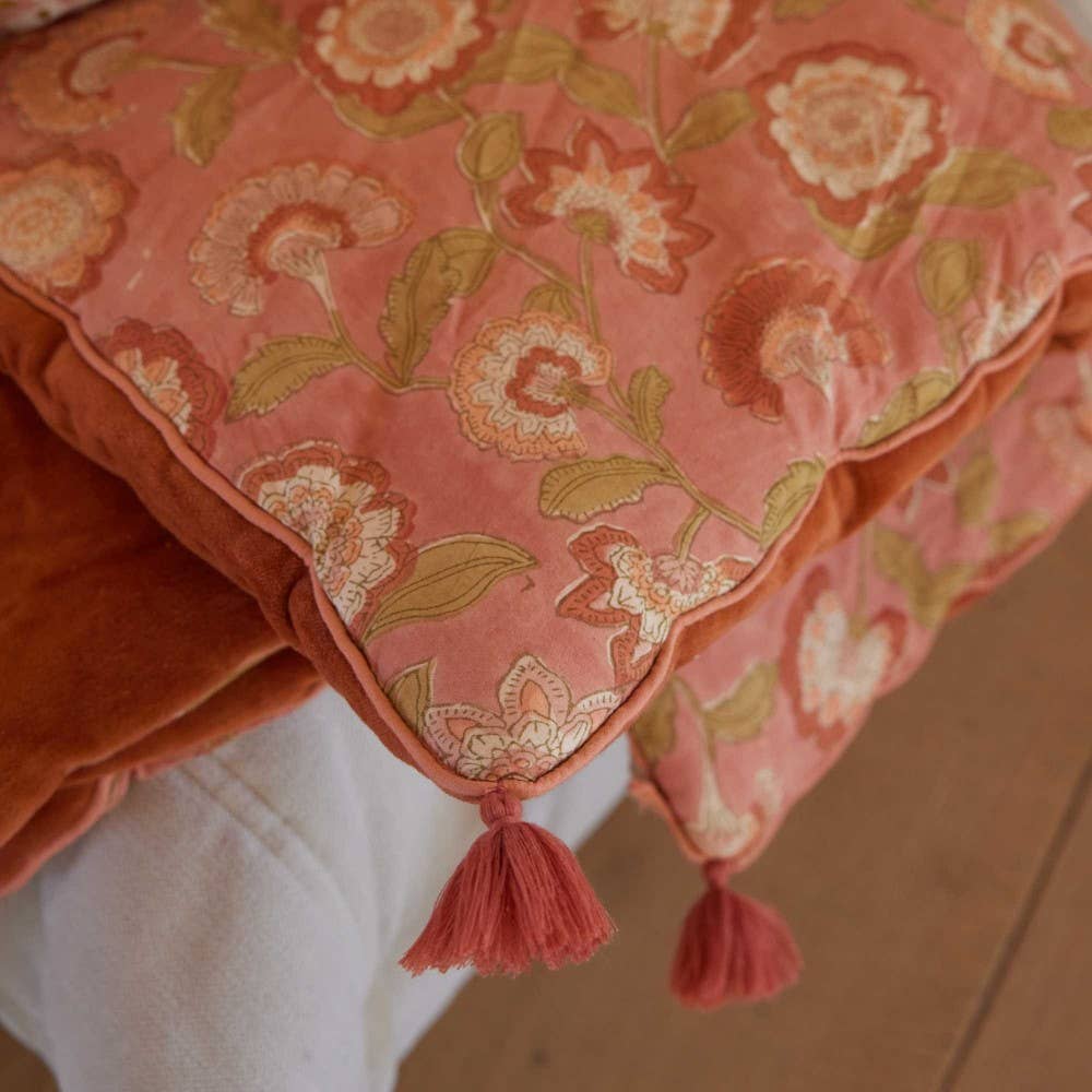 Decorative pillow with floral pattern and tassels on a wooden surface