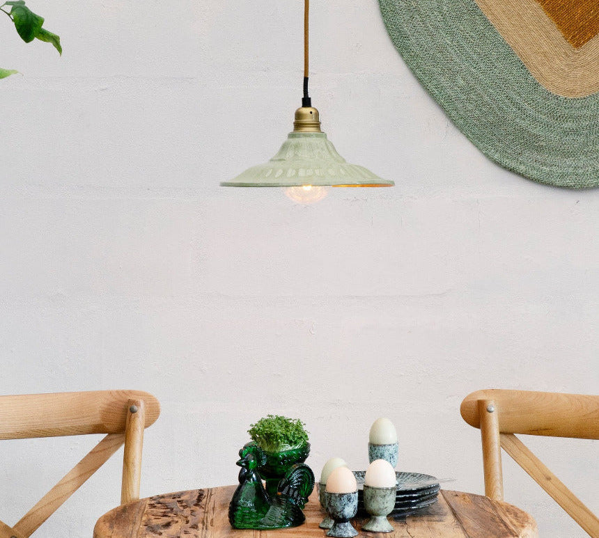 Dining area with wooden table and chairs, plants, and a light green enamel pendant light 
