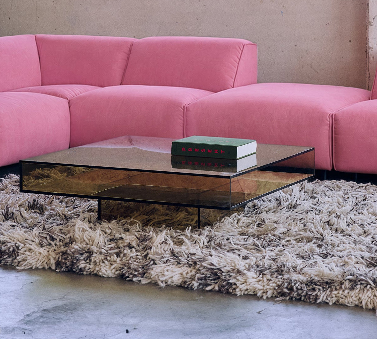 A pink modular sectional sofa arranged in an industrial loft setting with concrete columns, large windows, and a shag rug.