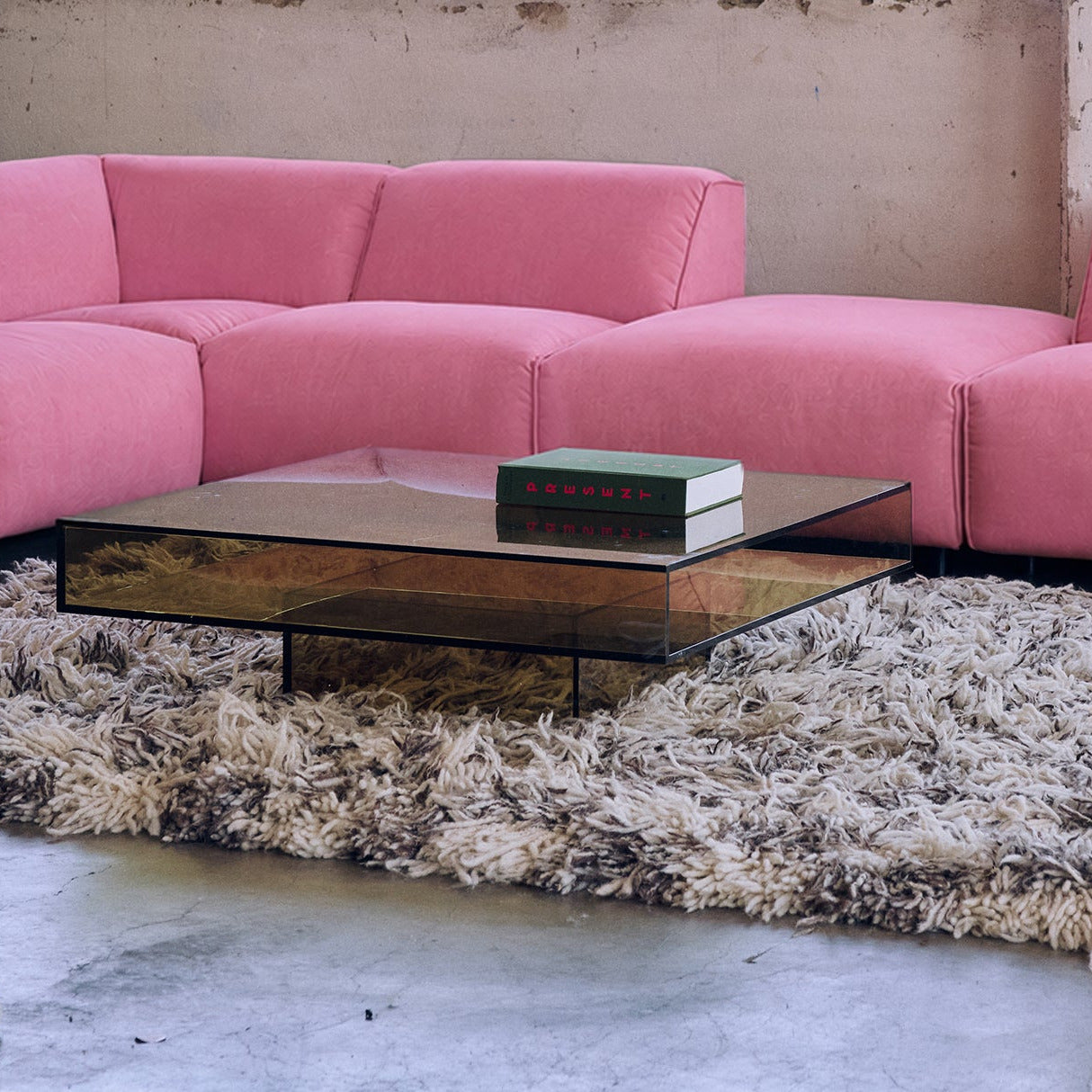 A pink modular sectional sofa arranged in an industrial loft setting with concrete columns, large windows, and a shag rug.