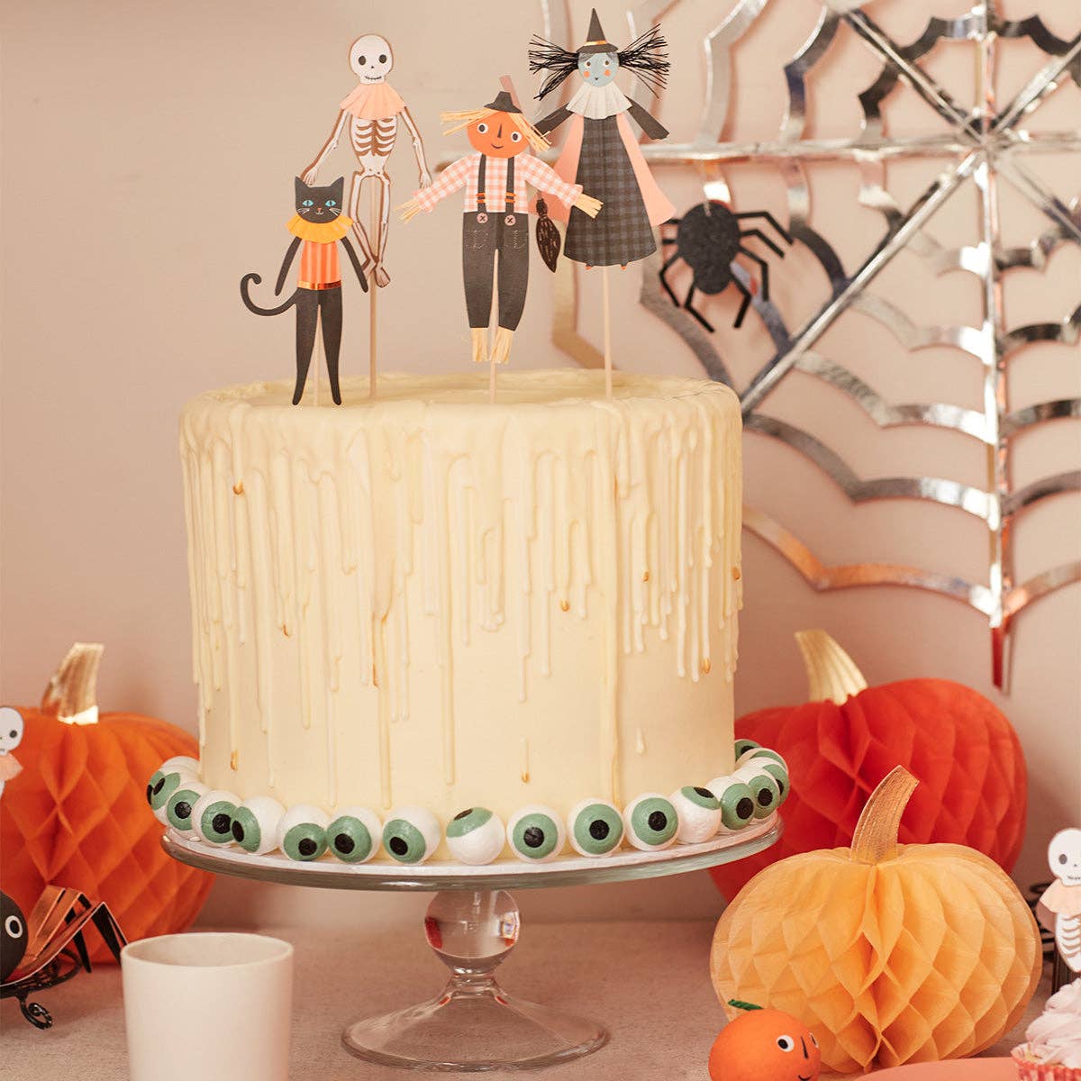 Halloween-themed cake with decorative toppers and pumpkins on a table.