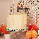 Halloween-themed cake with decorative toppers and pumpkins on a table.
