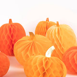 A group of orange and yellow honeycomb paper pumpkins with small faux stems, arranged on a clean white background.
