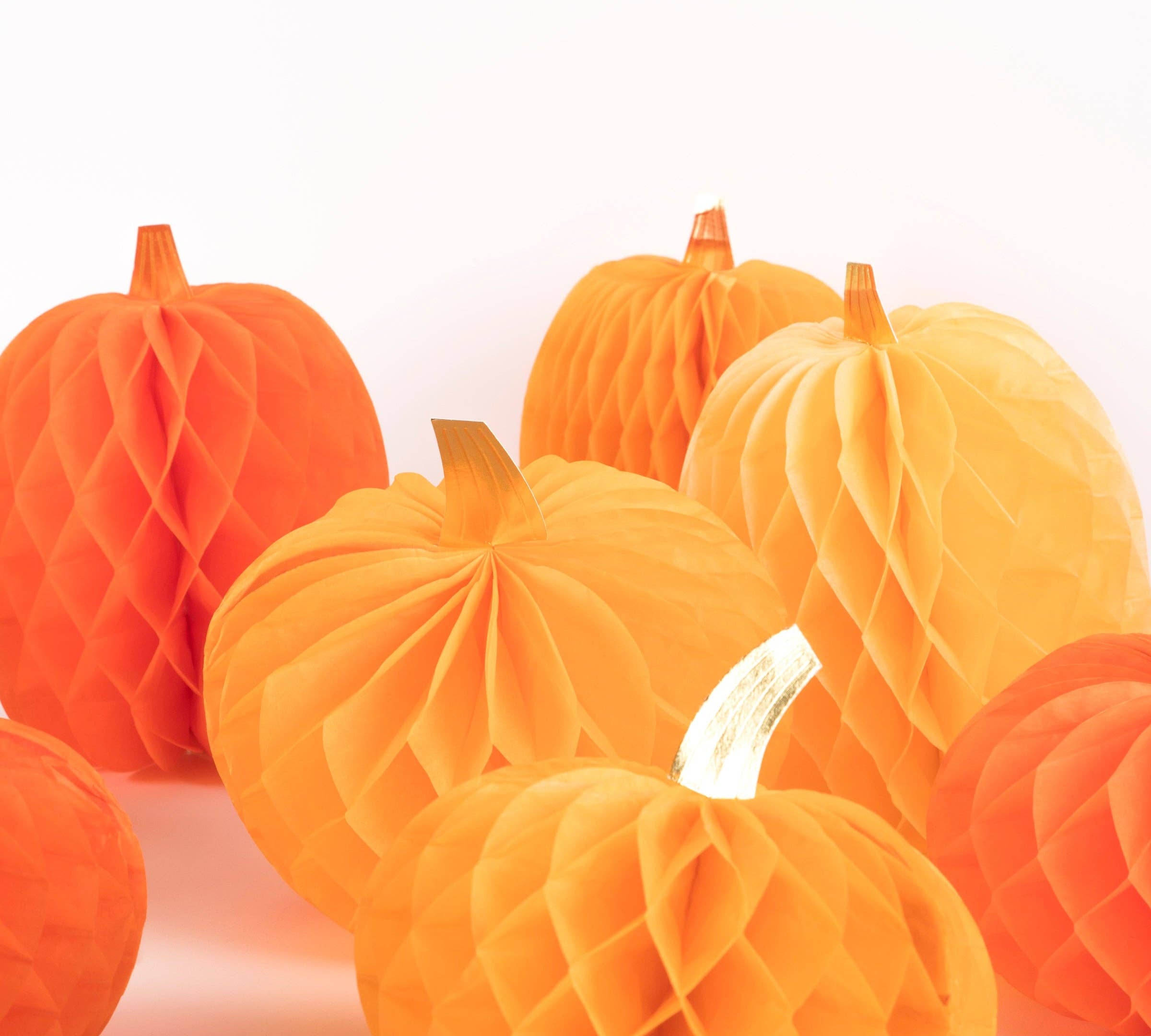 A group of orange and yellow honeycomb paper pumpkins with small faux stems, arranged on a clean white background.