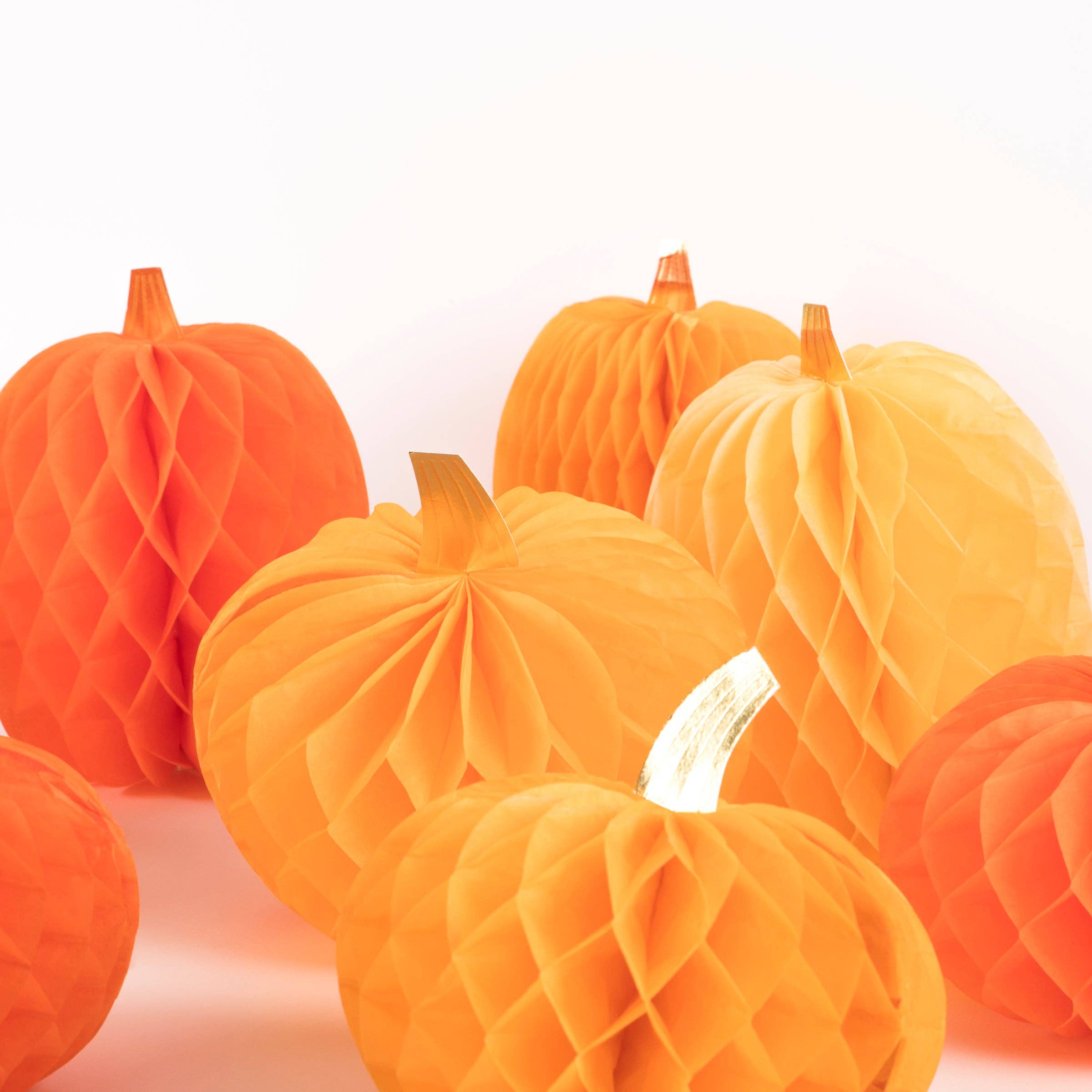 A group of orange and yellow honeycomb paper pumpkins with small faux stems, arranged on a clean white background.