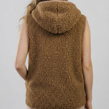 A woman viewed from the back wearing a sleeveless brown sherpa fleece hooded vest against a light gray studio background.