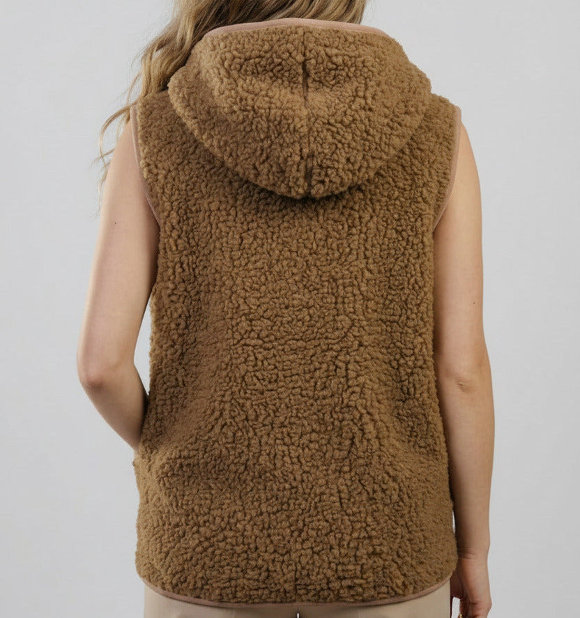 A woman viewed from the back wearing a sleeveless brown sherpa fleece hooded vest against a light gray studio background.