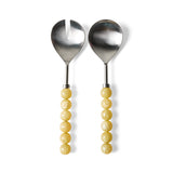 Two metal salad serving utensils with yellow beaded handles, one a spoon and one a fork with a vertical notch, shown on a white background.