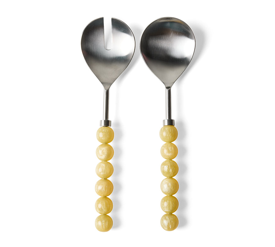 Two metal salad serving utensils with yellow beaded handles, one a spoon and one a fork with a vertical notch, shown on a white background.