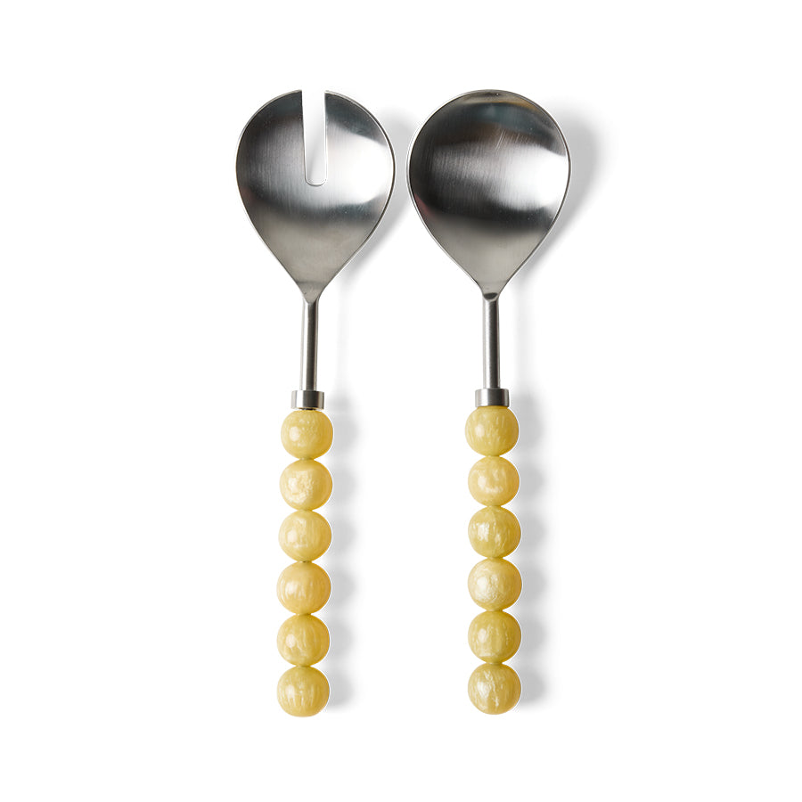 Two metal salad serving utensils with yellow beaded handles, one a spoon and one a fork with a vertical notch, shown on a white background.