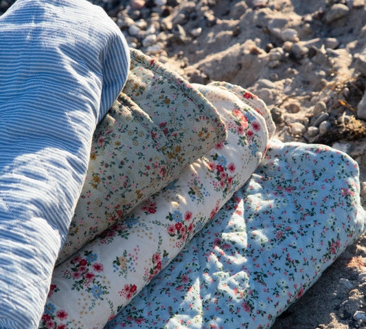 Floral-patterned quilt rolled up on a sandy surface