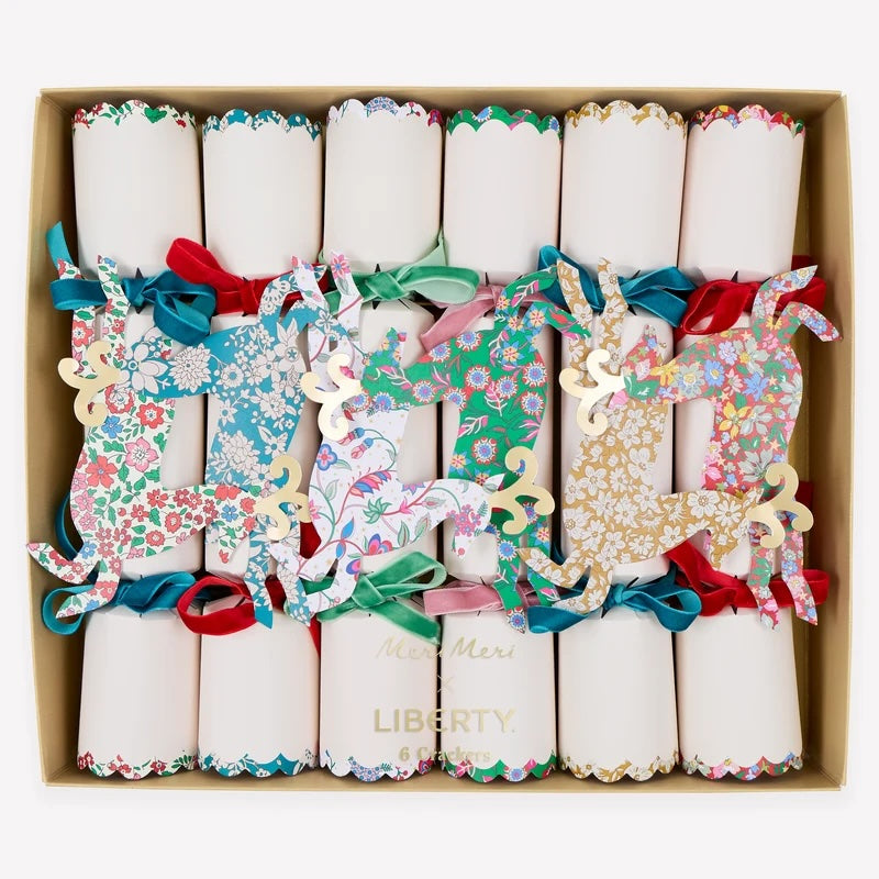 A boxed set of Christmas crackers ornaments arranged in a square cardboard tray. Each cracker is decorated with a different colorful floral and whimsical pattern, tied with a ribbon, and some have gold foil text.