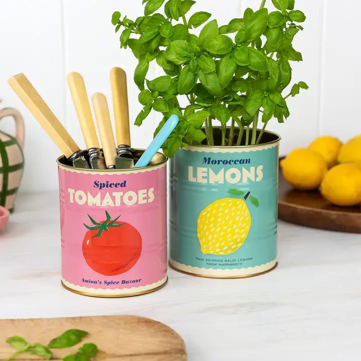 Two repurposed canisters with planters and kitchen utensils on a white surface.