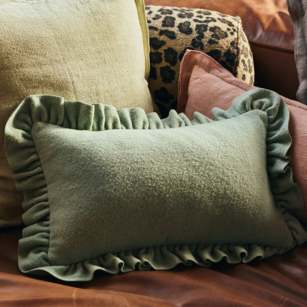 An mint green rectangular cushion with ruffled trim, styled on a brown leather sofa alongside other decorative pillows.