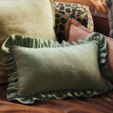 An mint green rectangular cushion with ruffled trim, styled on a brown leather sofa alongside other decorative pillows.