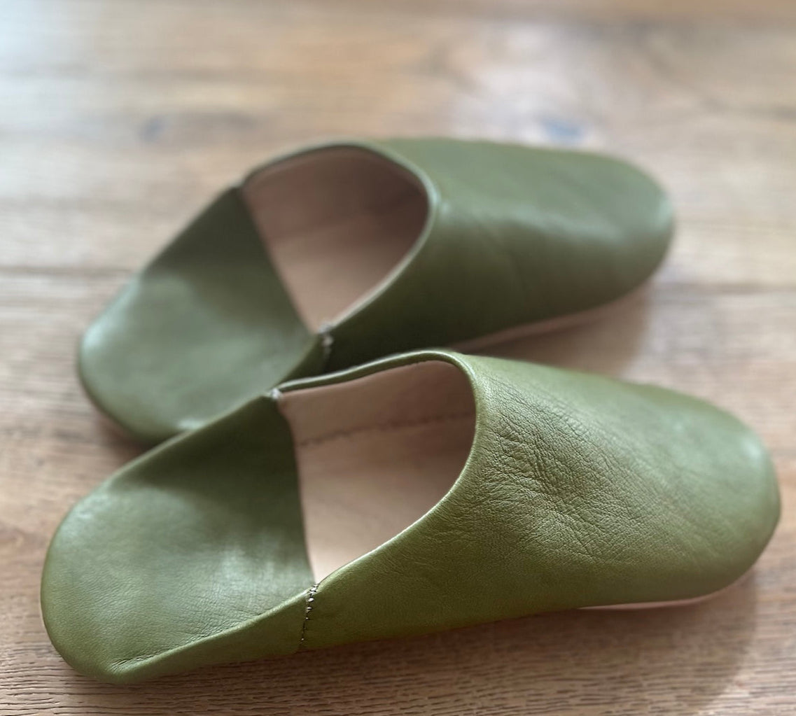 Pair of green leather slippers on a wooden surface