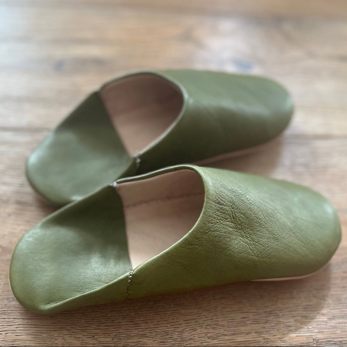 Pair of green leather slippers on a wooden surface