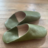 Pair of green leather slippers on a wooden surface