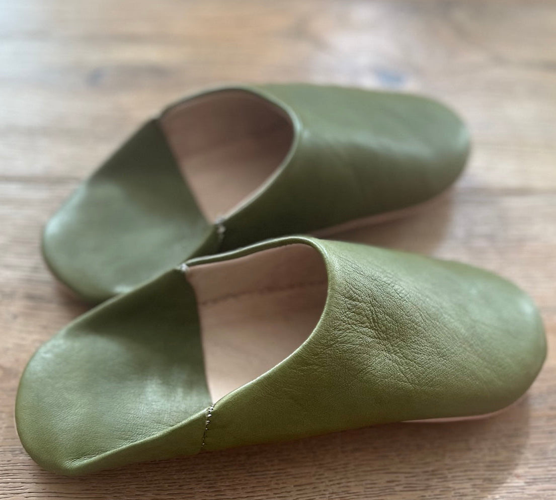 Pair of green leather slippers on a wooden surface