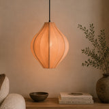 pink pendant lamp hanging above a table with books and a plant in a dimly lit room.