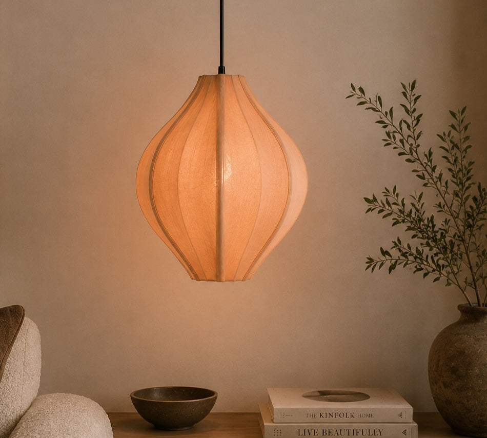 pink pendant lamp hanging above a table with books and a plant in a dimly lit room.