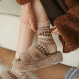 Person wearing patterned socks with fluffy cuffs, sitting on a wooden floor.