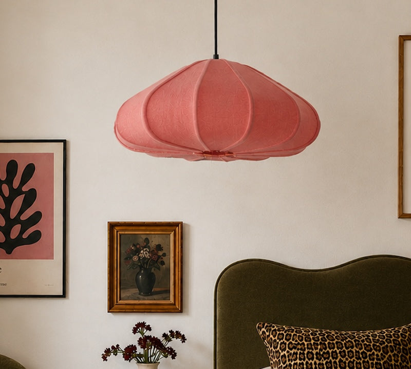 Pink pendant lamp hanging above a bed with decorative elements on a wall.