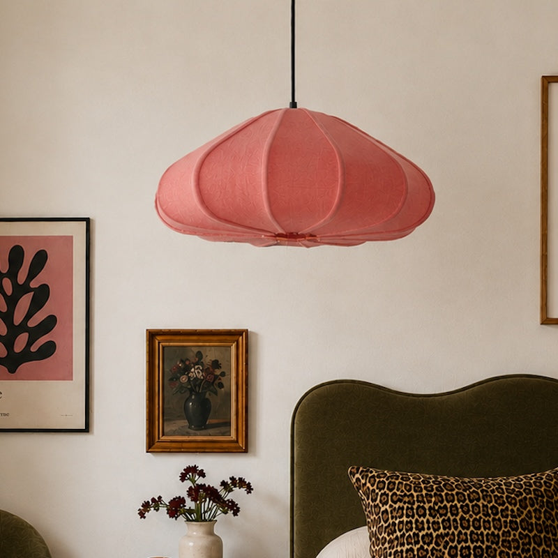 Pink pendant lamp hanging above a bed with decorative elements on a wall.